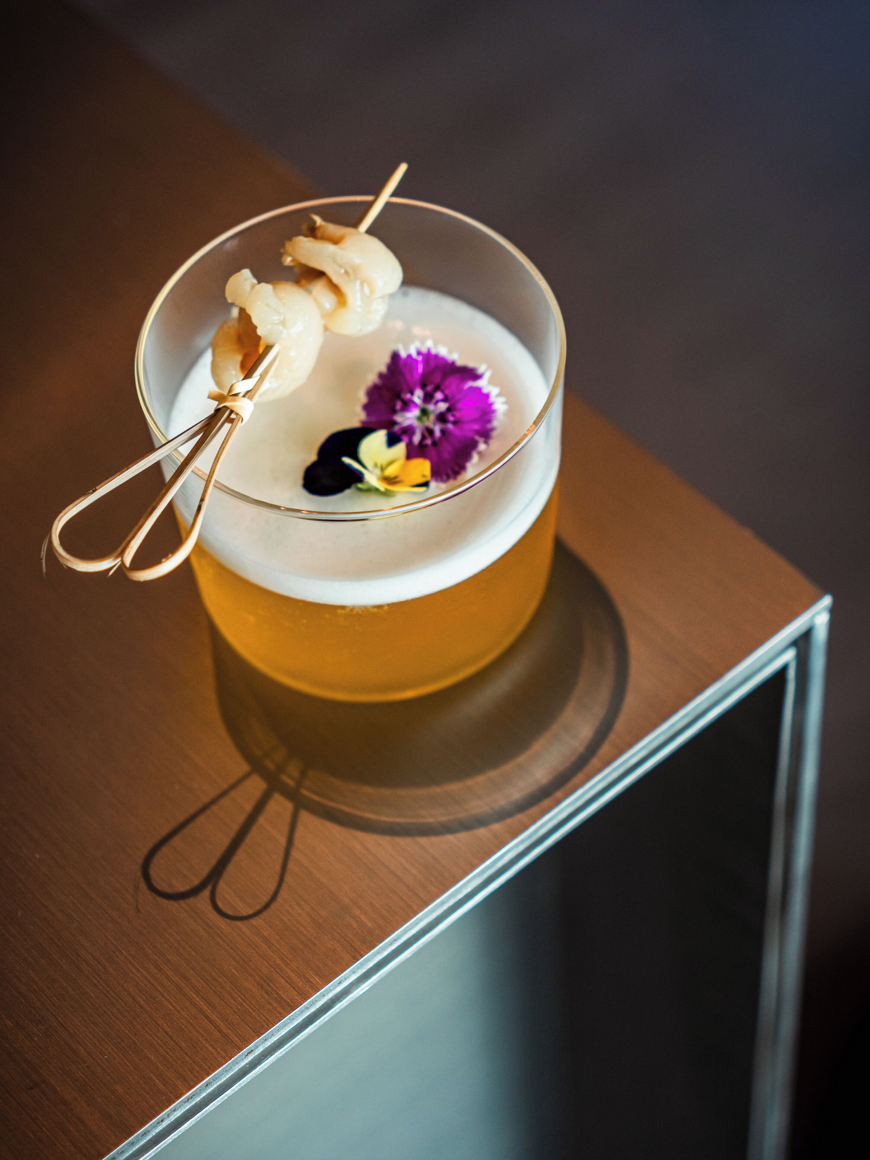 A cocktail with a garnish and a flower on a glass.