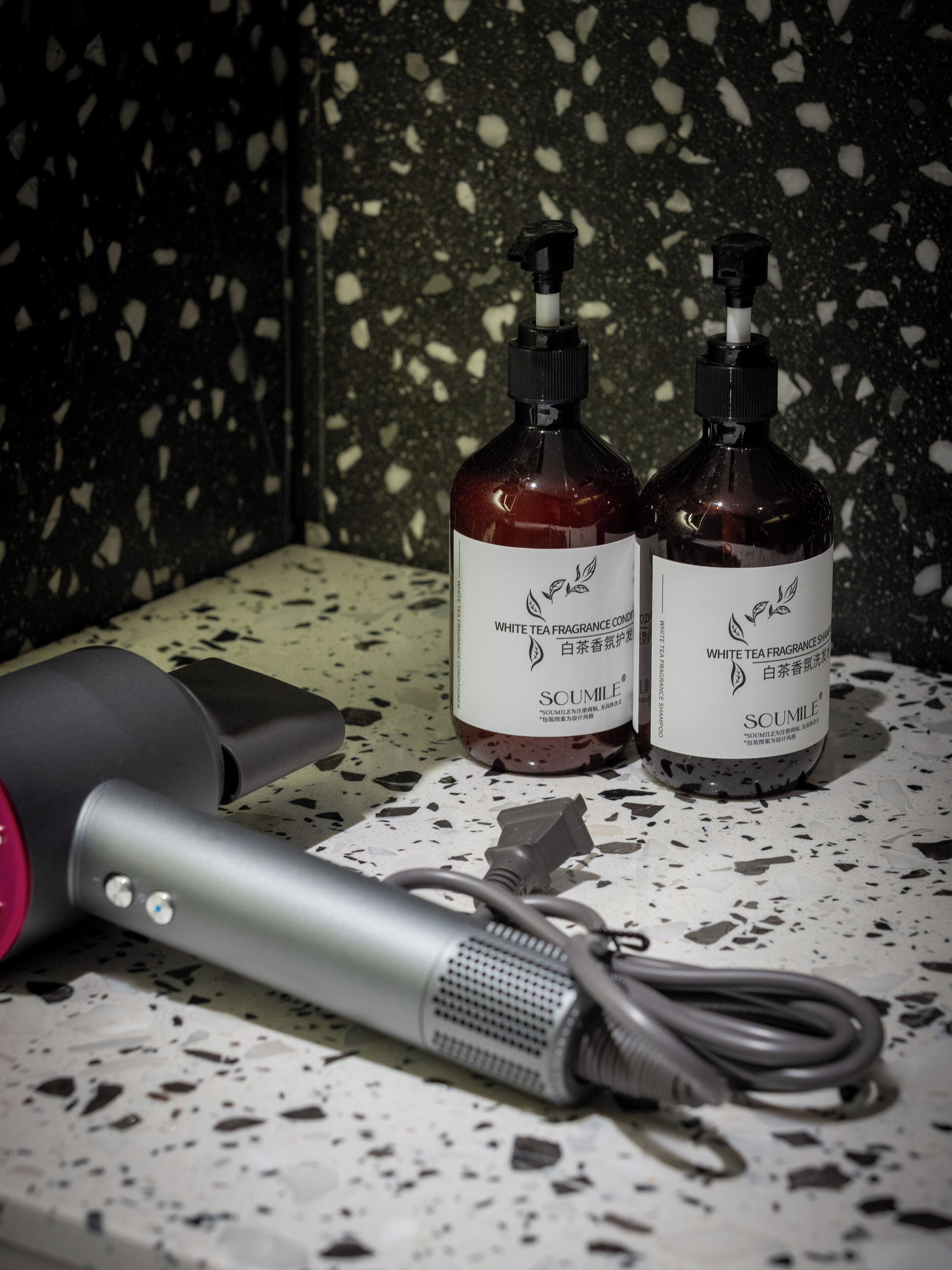 Two bottles of white tea fragrance conditioner and a hairdryer on a speckled countertop.