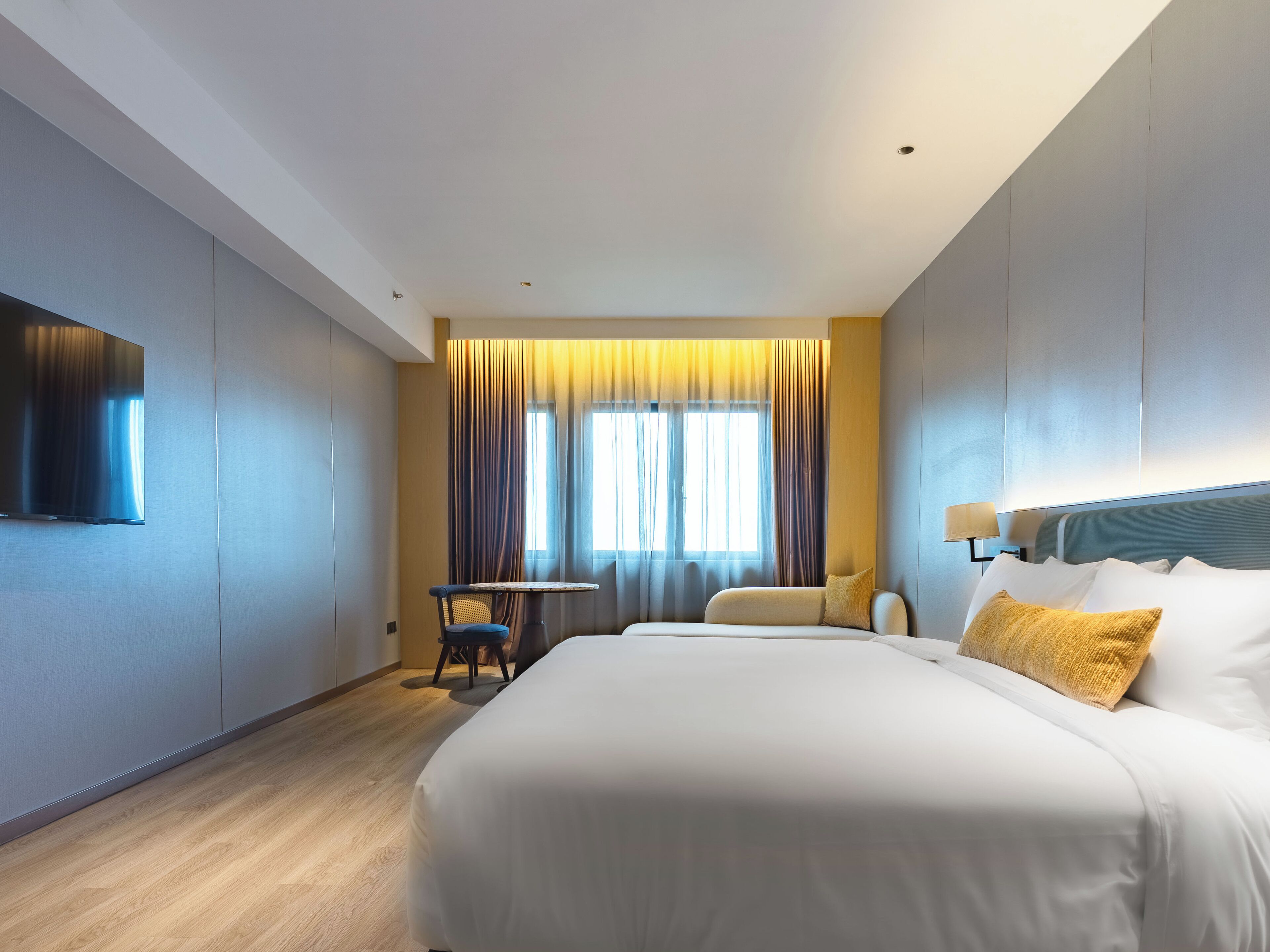 A modern hotel room with a large bed, a small table, and a TV mounted on the wall.
