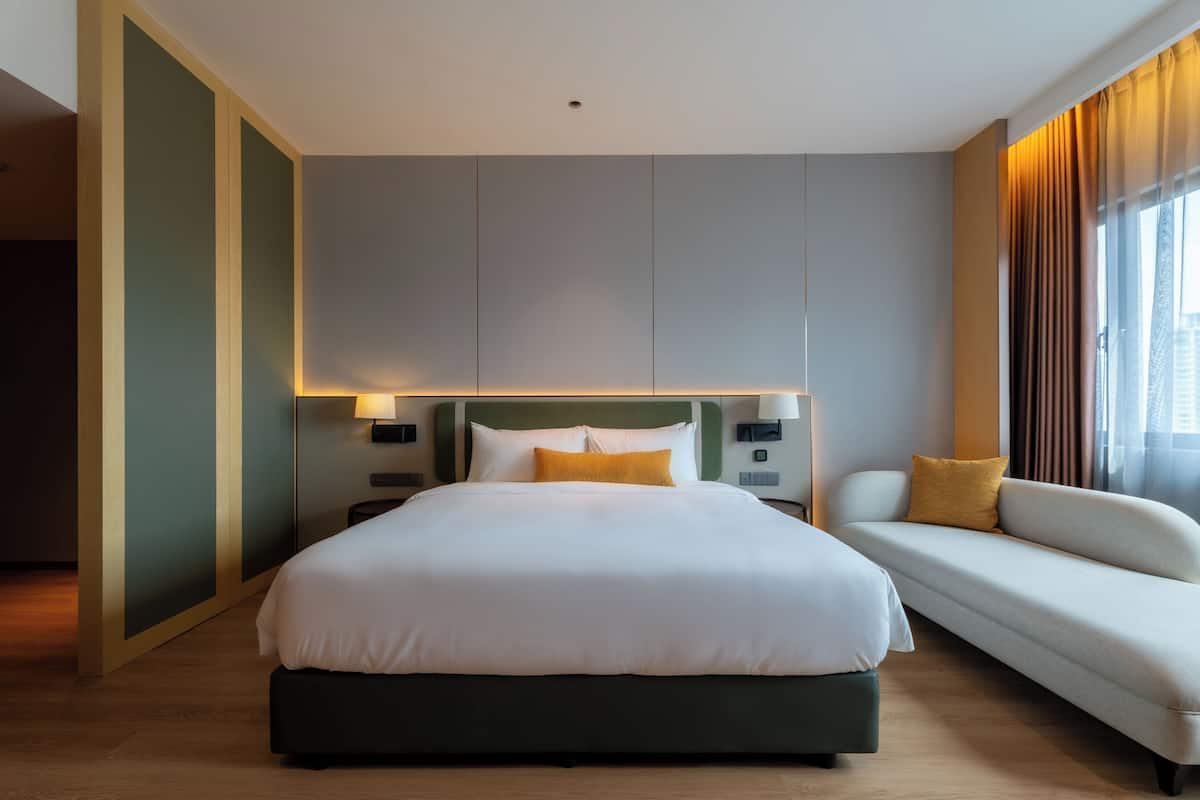 Une chambre d’hôtel moderne, dotée d’un grand lit, d’un canapé et d’une table de chevet avec une lampe.