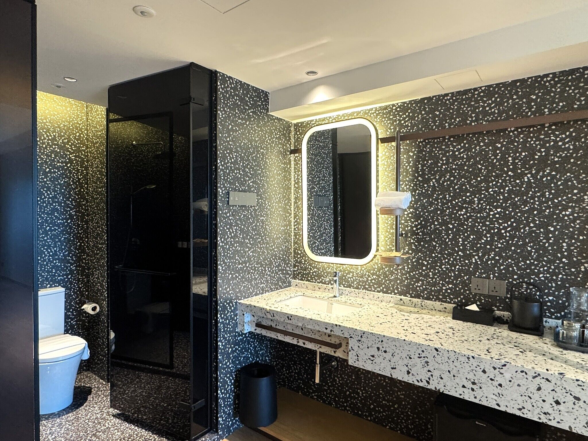 Un baño moderno con un revoque salpicado, un espejo grande y una encimera con lavamanos y tocador.