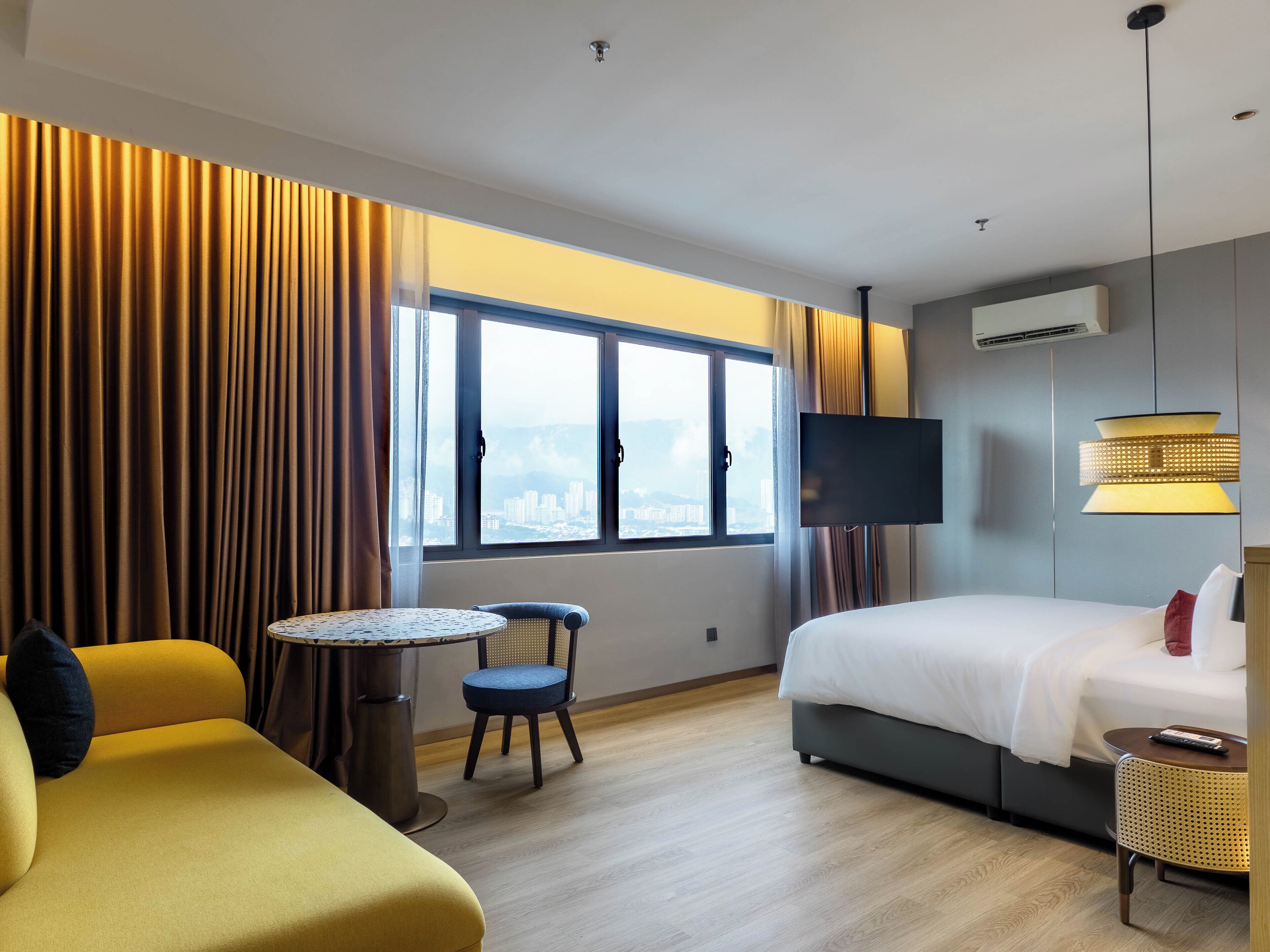 A hotel room with a bed, a sofa, a chair, a small table, a TV, and a window with curtains.
