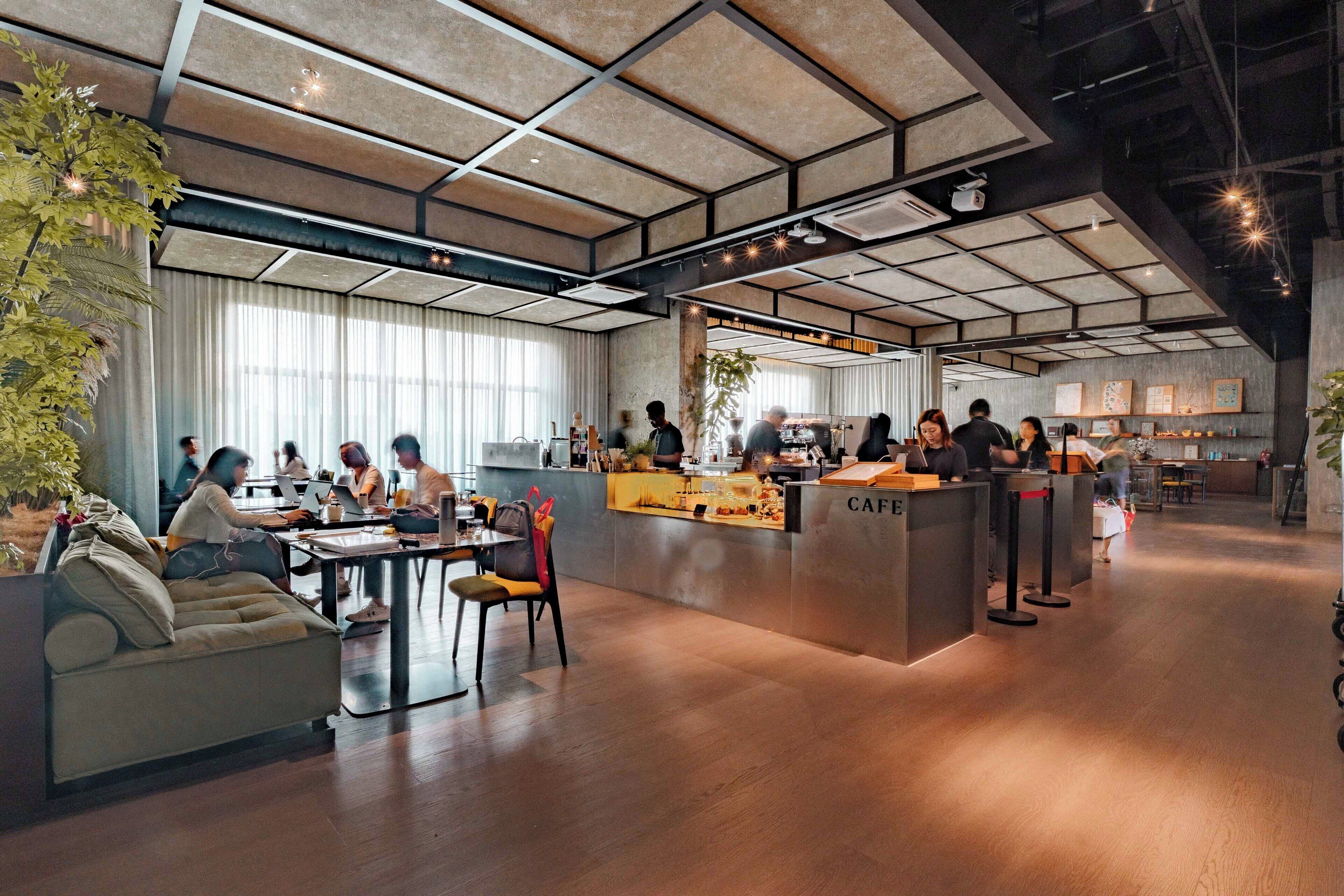 A modern cafe with a central counter, seating area, and large windows.