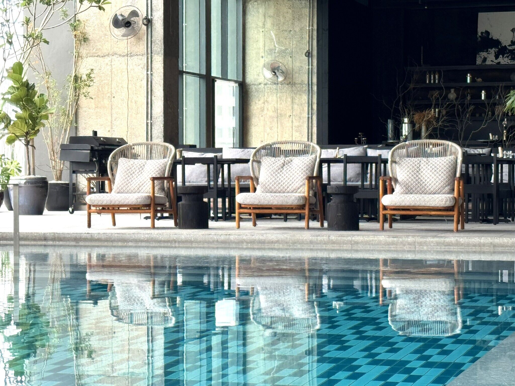 A poolside area with three wicker chairs and a piano, reflecting in the pool.