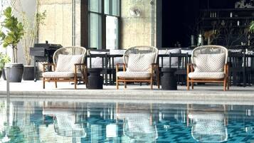 A poolside area with three wicker chairs and a piano, reflecting in the pool.