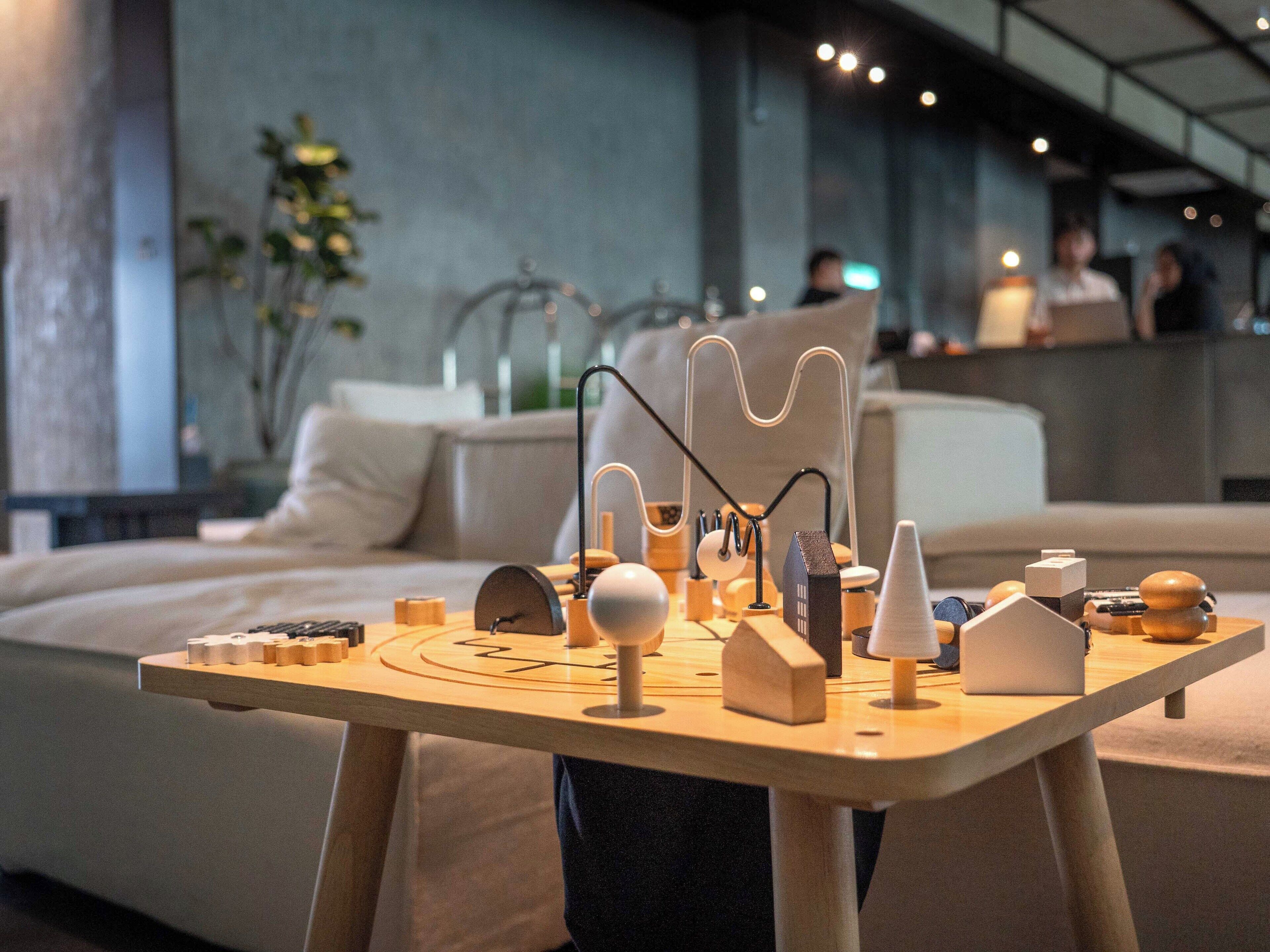 A modern hotel room with a minimalist design, featuring a wooden table with various objects and a sofa in the background.