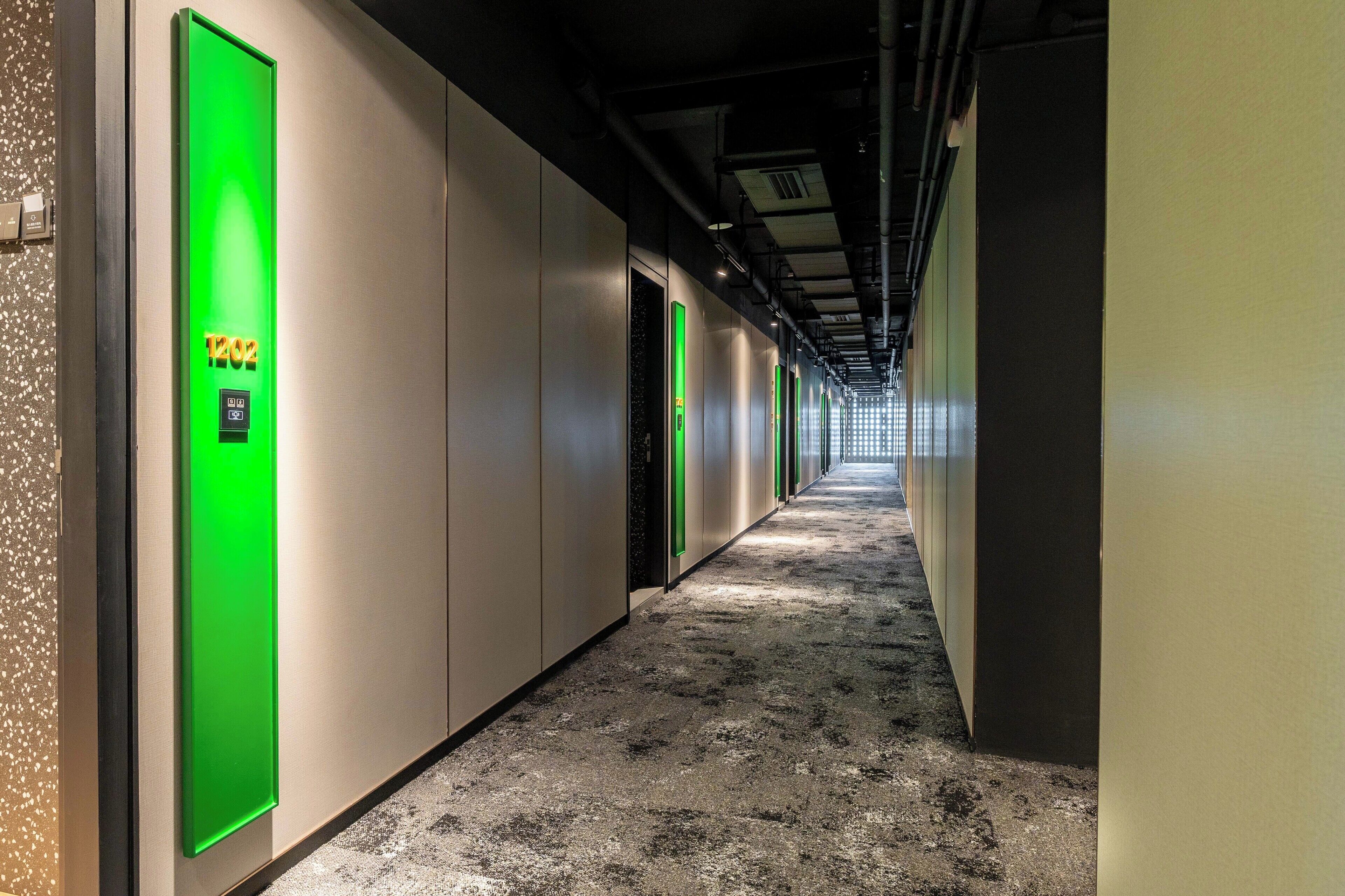 A hallway with green-lit elevator doors, a speckled floor, and a long corridor with doors on both sides.