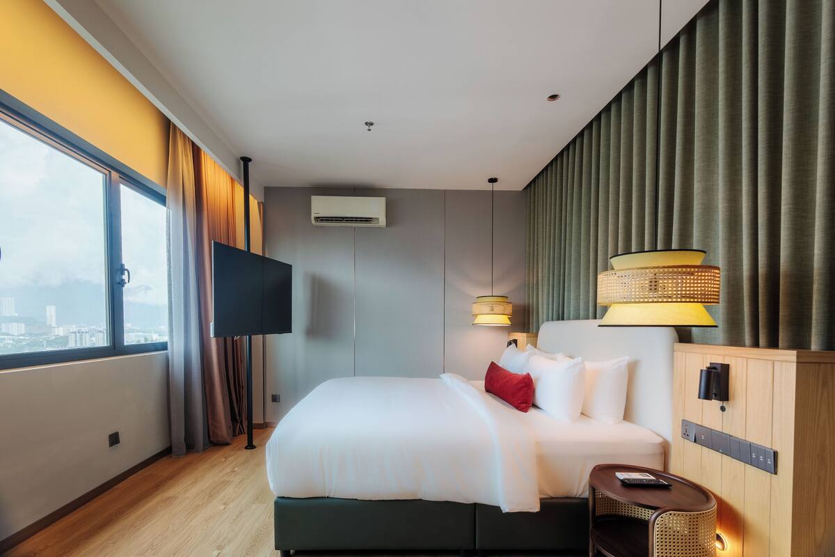 Une chambre d’hôtel moderne avec un grand lit, une télévision, une table de chevet en bois et une vue sur la ville par la fenêtre.