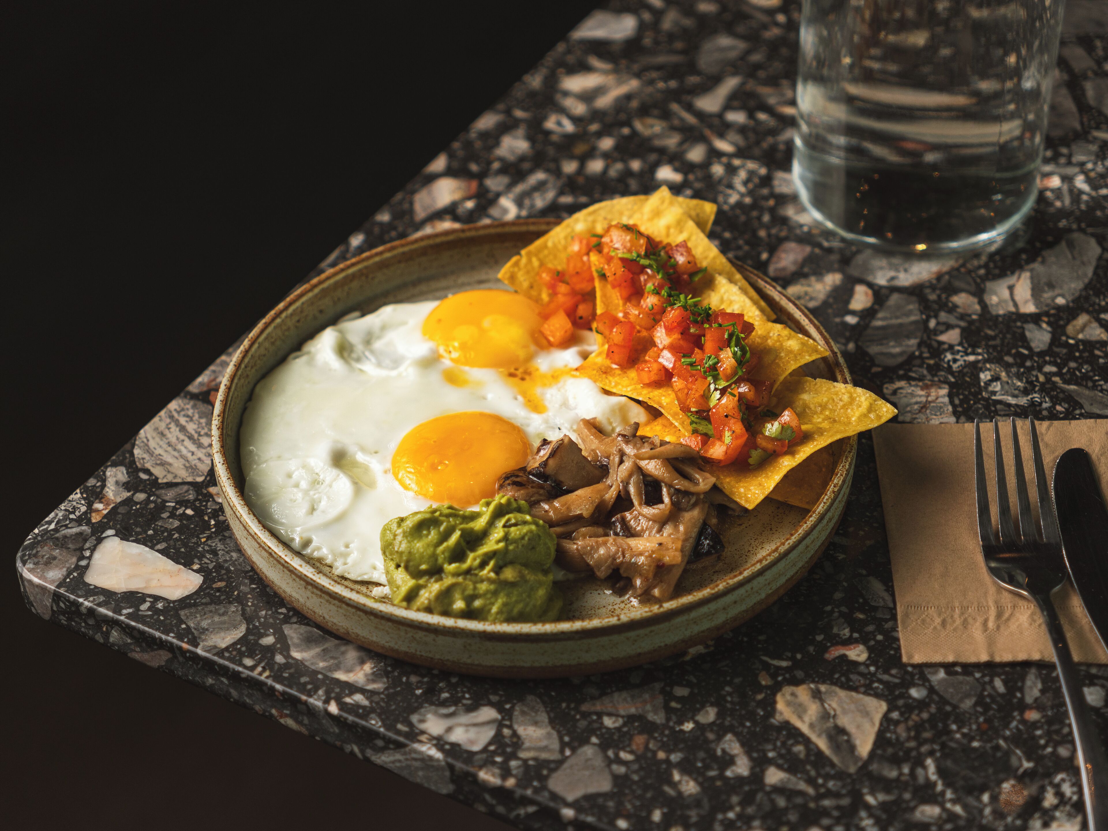 A breakfast plate with eggs, guacamole, and salsa on a ceramic plate on a marble table.
