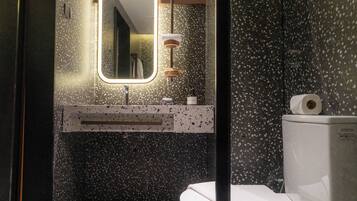 A modern bathroom with a speckled floor, a mirror with a light, a toilet, and a sink with a towel hanging on it.