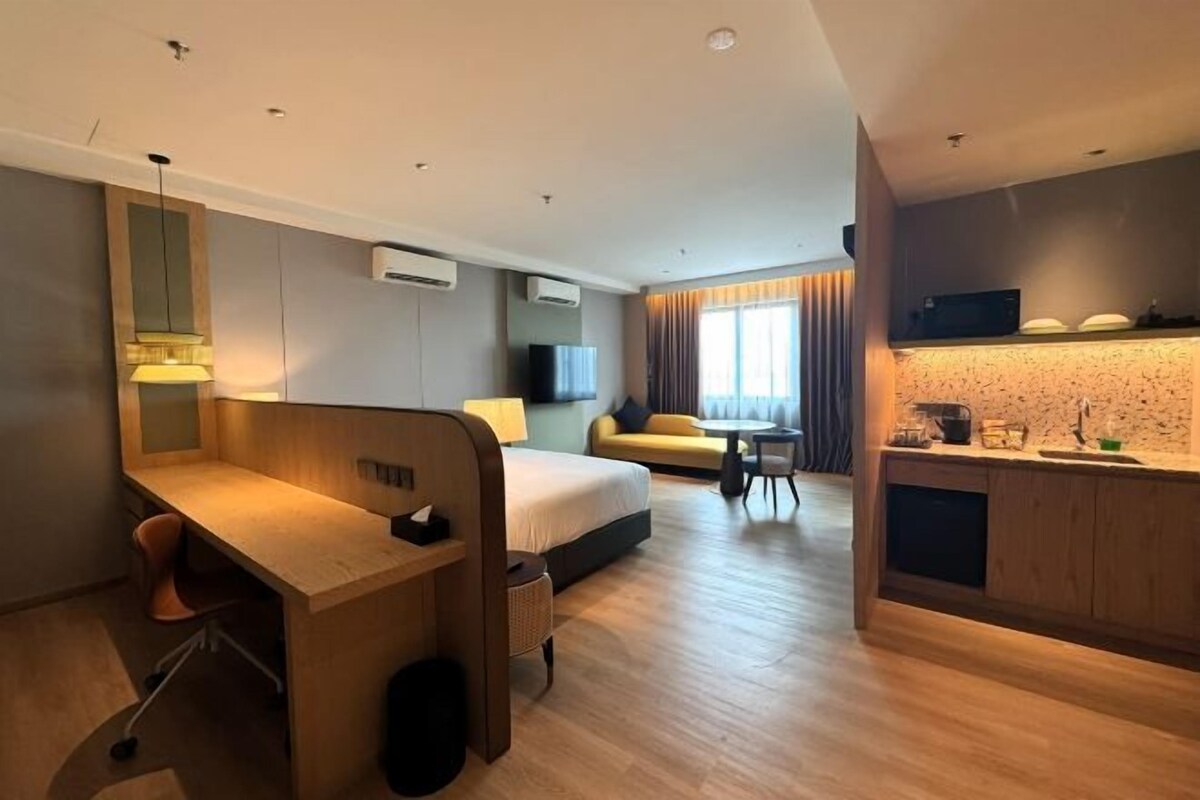 Una habitación de hotel moderna con un escritorio de madera, una cama, un sofá, una mesita y una kitchenette.
