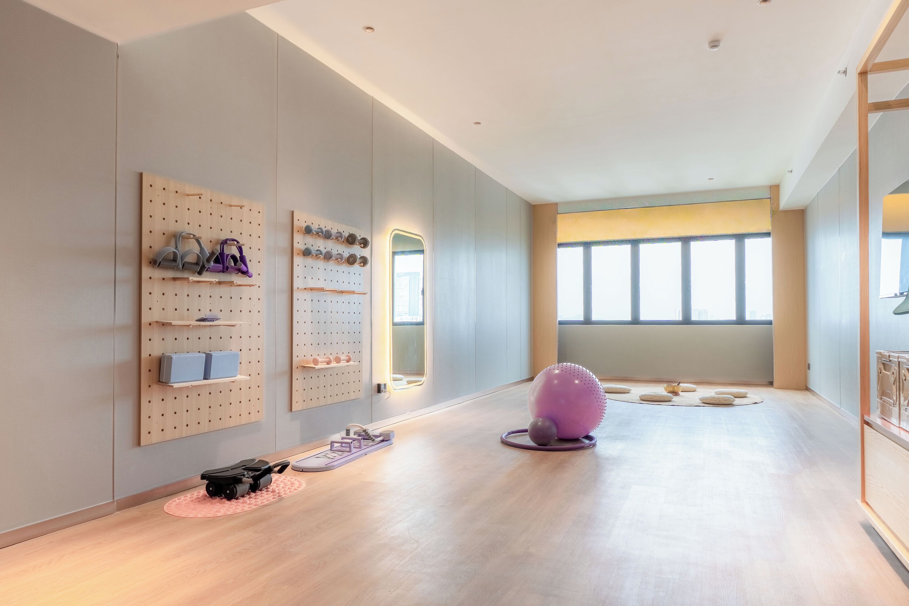 A spacious room with a wooden floor, a large window, and wall-mounted exercise equipment.