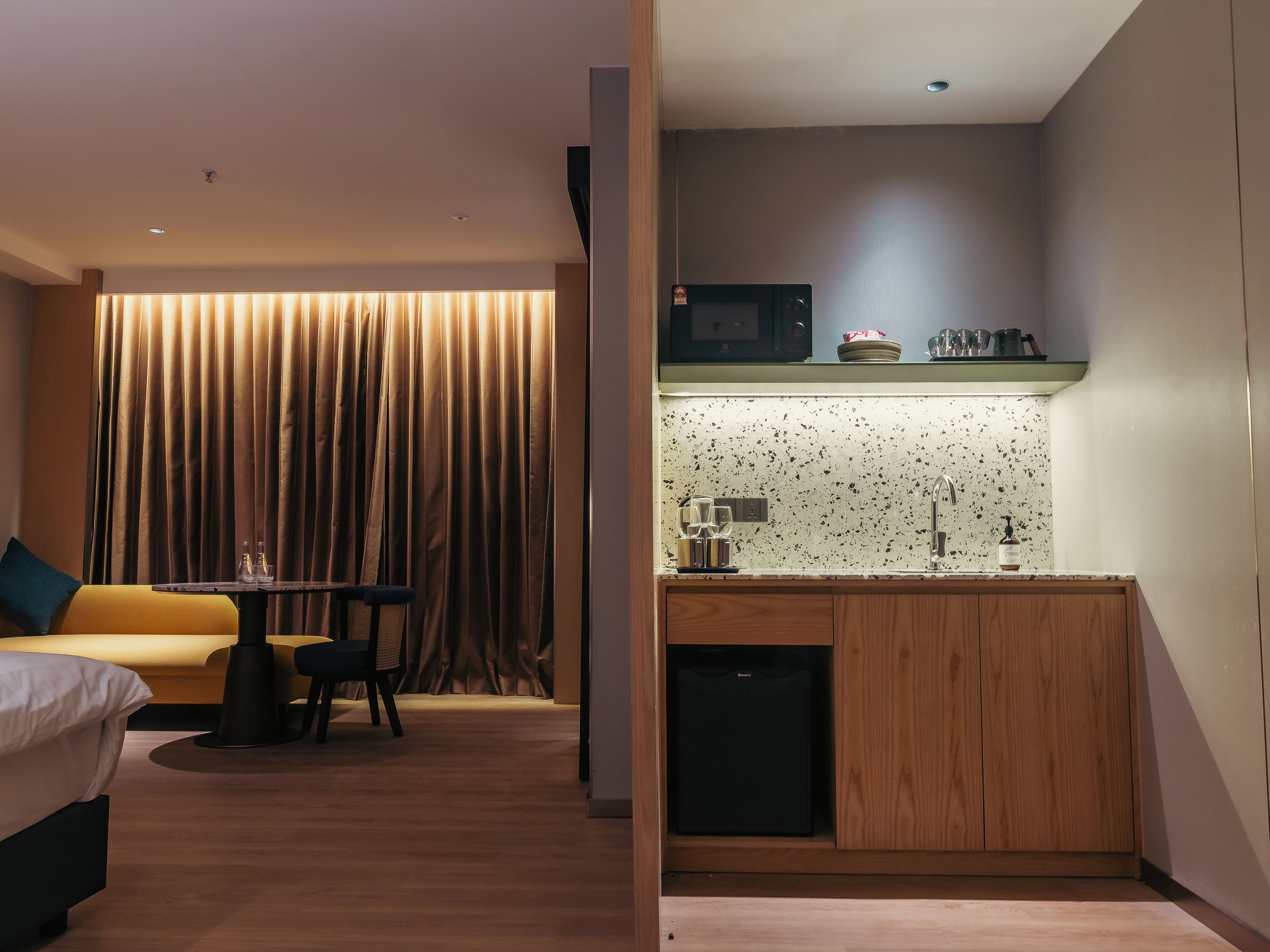 Ein modernes Hotelzimmer mit Holzboden, einer Couch, einem Esstisch und einer Küchenzeile mit Mikrowelle und Spüle.