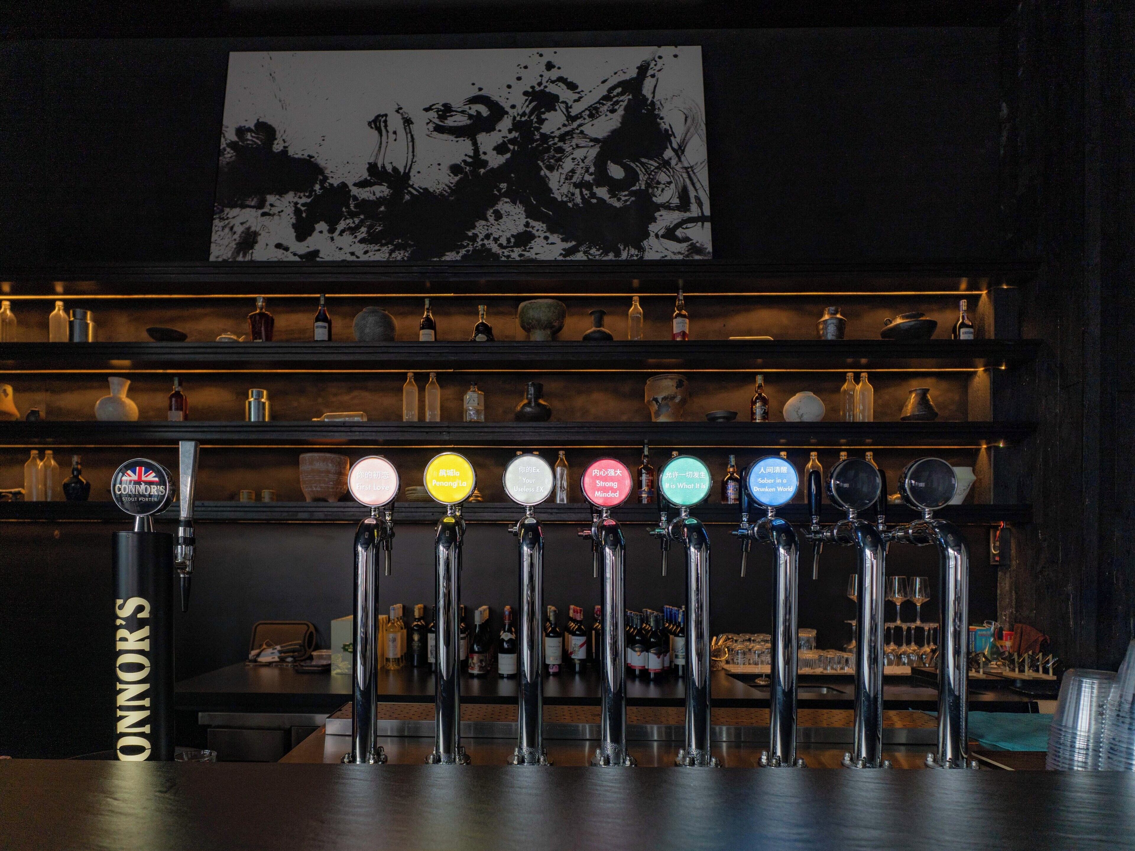 Un bar con varias llaves de cerveza etiquetadas con diferentes nombres y una variedad de botellas en estanterías al fondo.