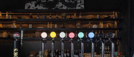 Un bar con varias llaves de cerveza etiquetadas con diferentes nombres y una variedad de botellas en estanterías al fondo.