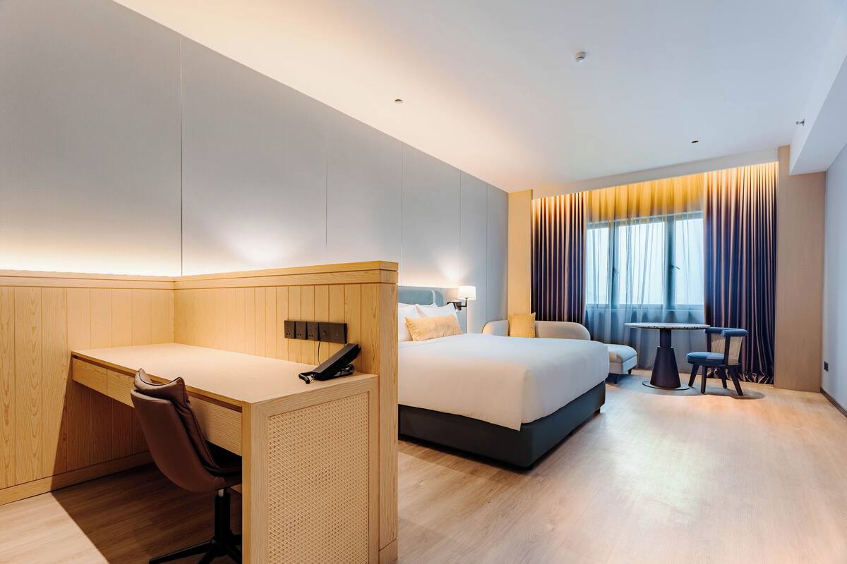 Une chambre d’hôtel moderne avec un bureau en bois, un lit, une petite table et une chaise.