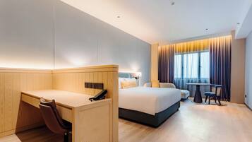 A modern hotel room with a wooden desk, a bed, a small table, and a chair.