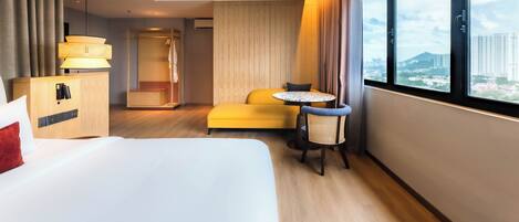 Habitación de hotel con cama, una mesita con silla, armario, escritorio y una ventana grande con vista a la ciudad.
