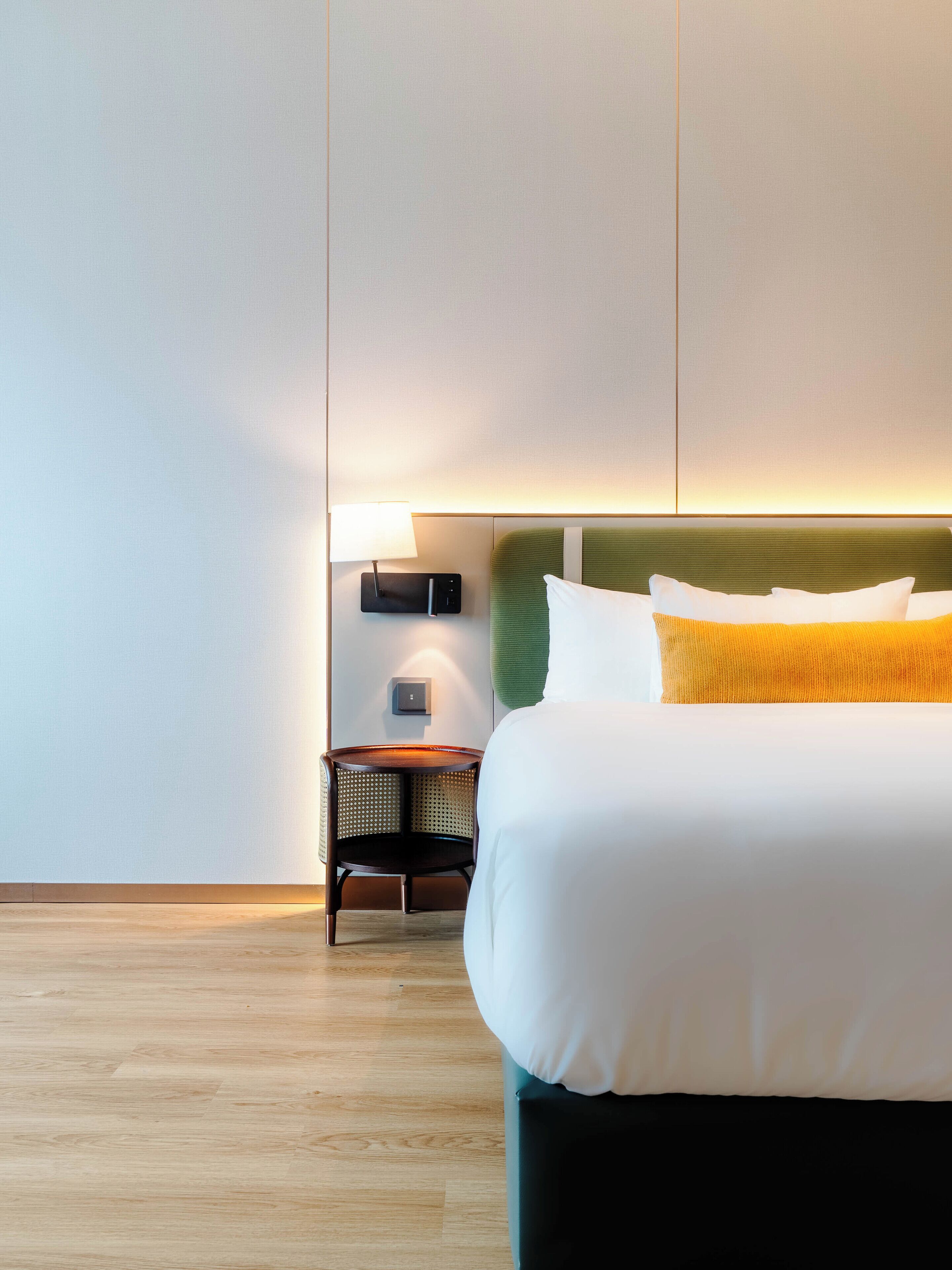 A hotel room with a bed, a nightstand, and a lamp.