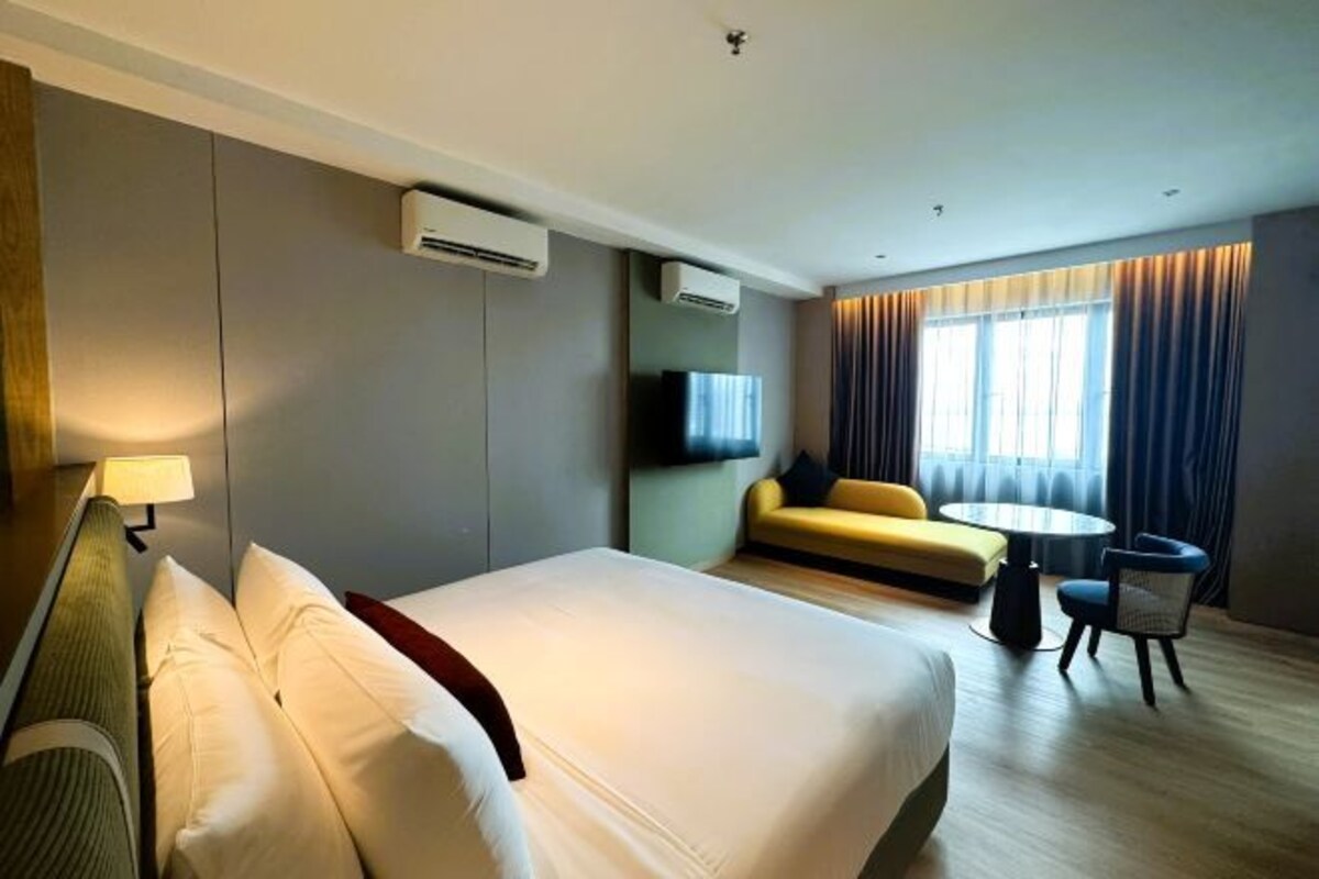 Une chambre d’hôtel avec un grand lit, un canapé, une petite table ronde et un téléviseur fixé au mur.