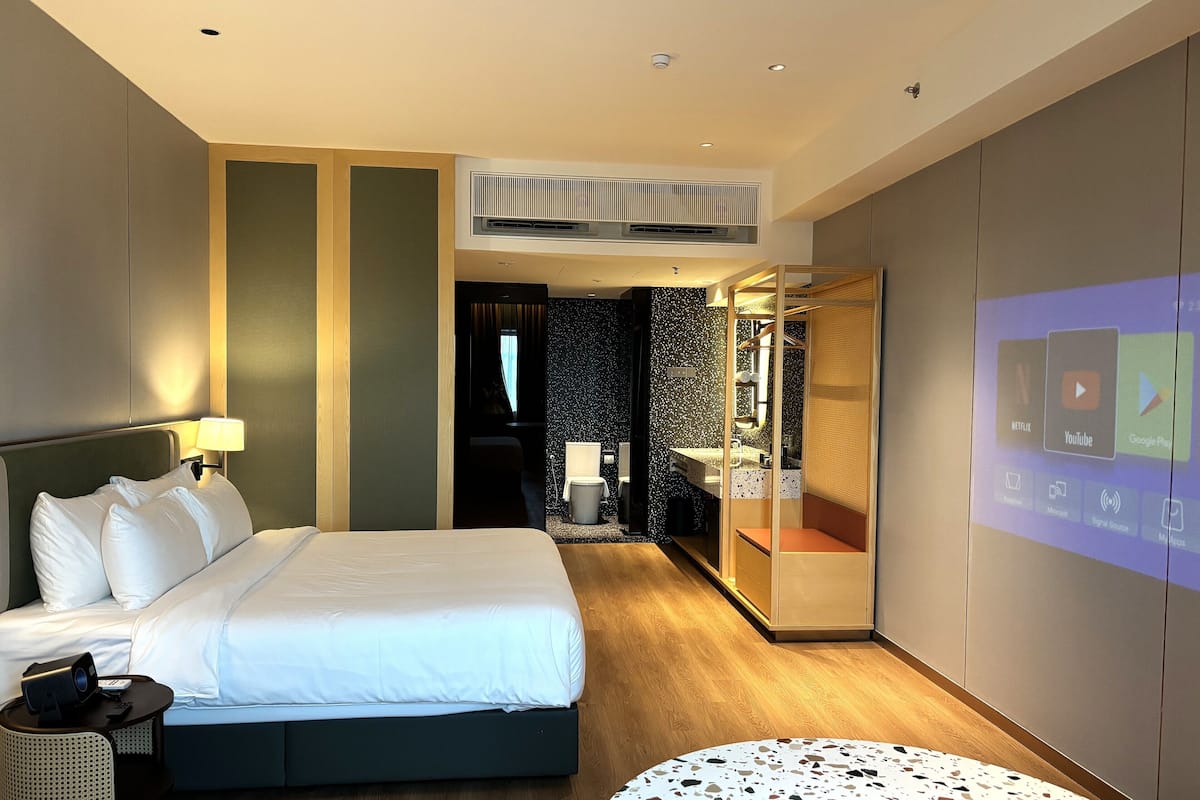 Une chambre d’hôtel moderne équipée d’un lit, d’une table de chevet et d’un écran fixé au mur affichant des icônes d’applications.