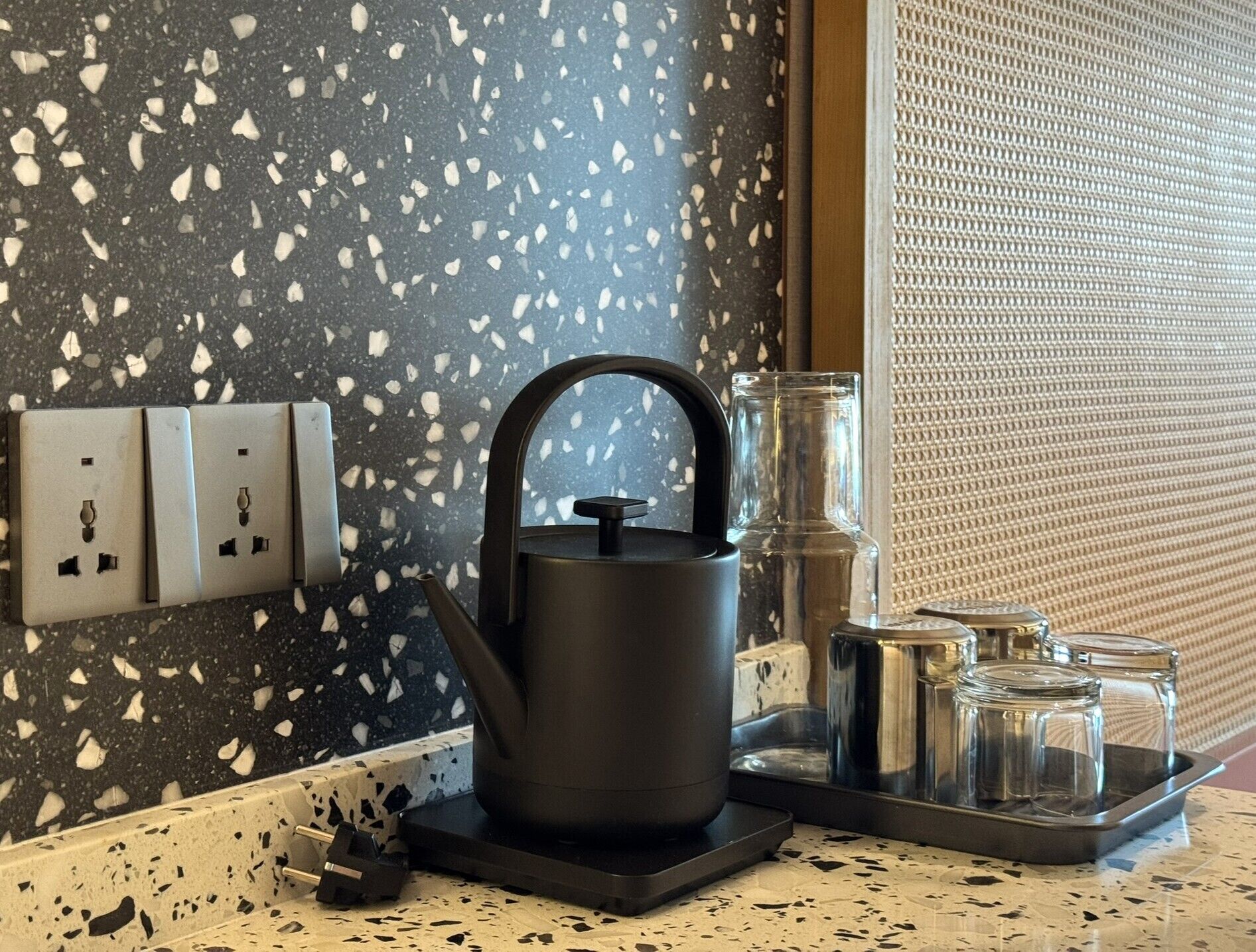 A kitchen counter with a black kettle, a glass carafe, and a tray with jars.
