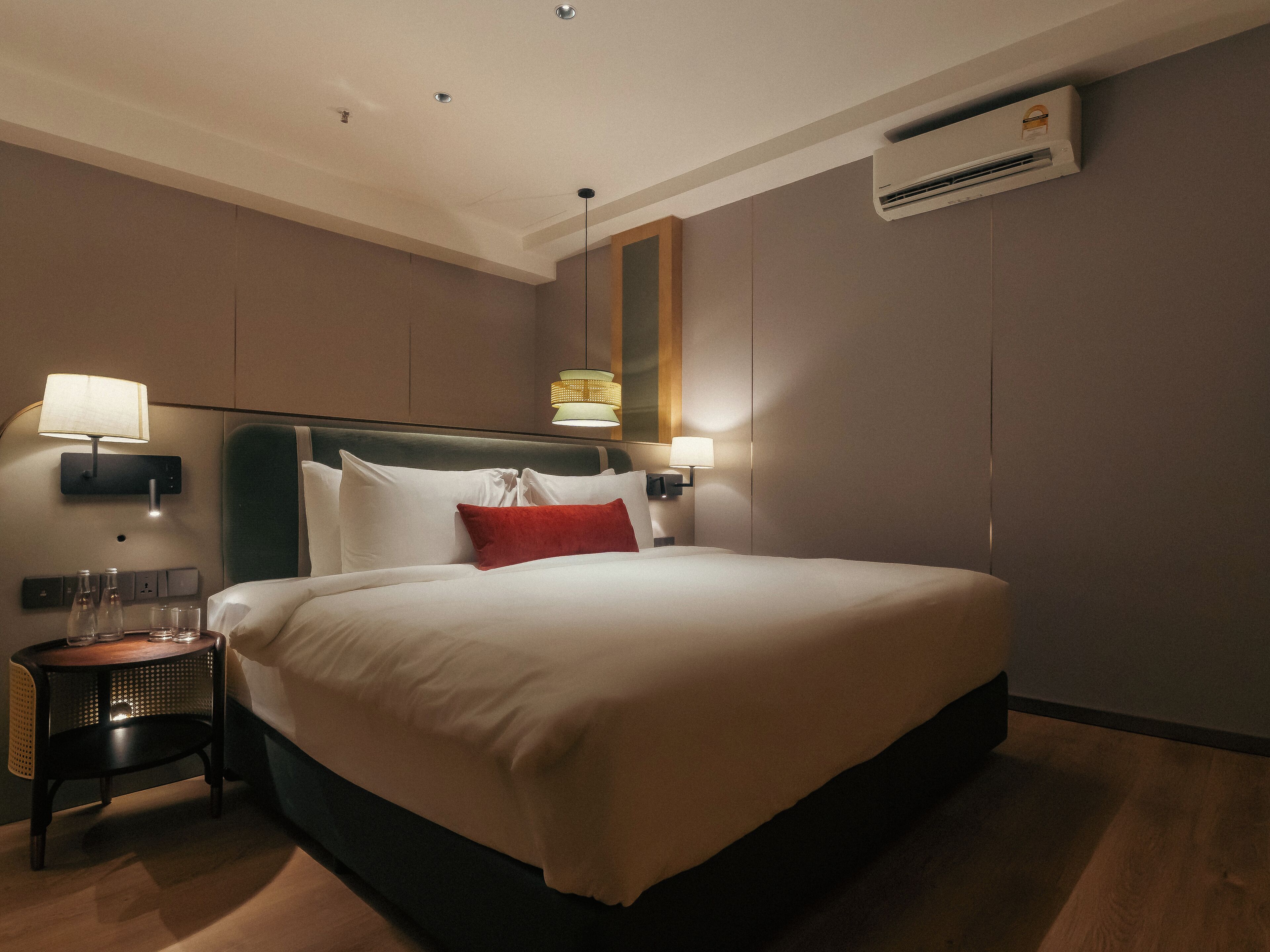 Une chambre d’hôtel avec un grand lit, deux lampes de chevet, une table de chevet avec des verres et un appareil de climatisation fixé au mur.