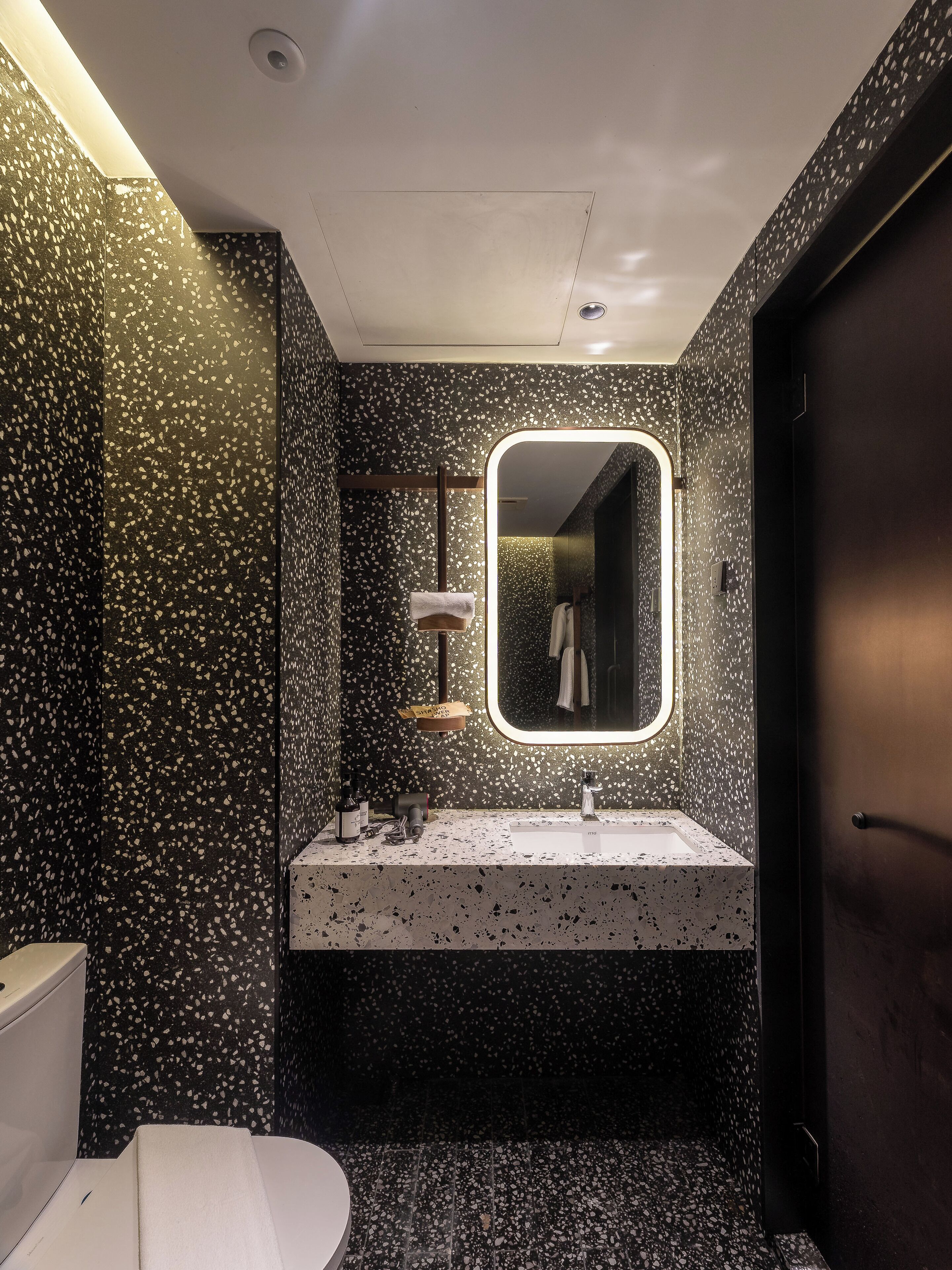 A modern bathroom with a speckled black and white tile design, a white sink, and a large mirror above it.
