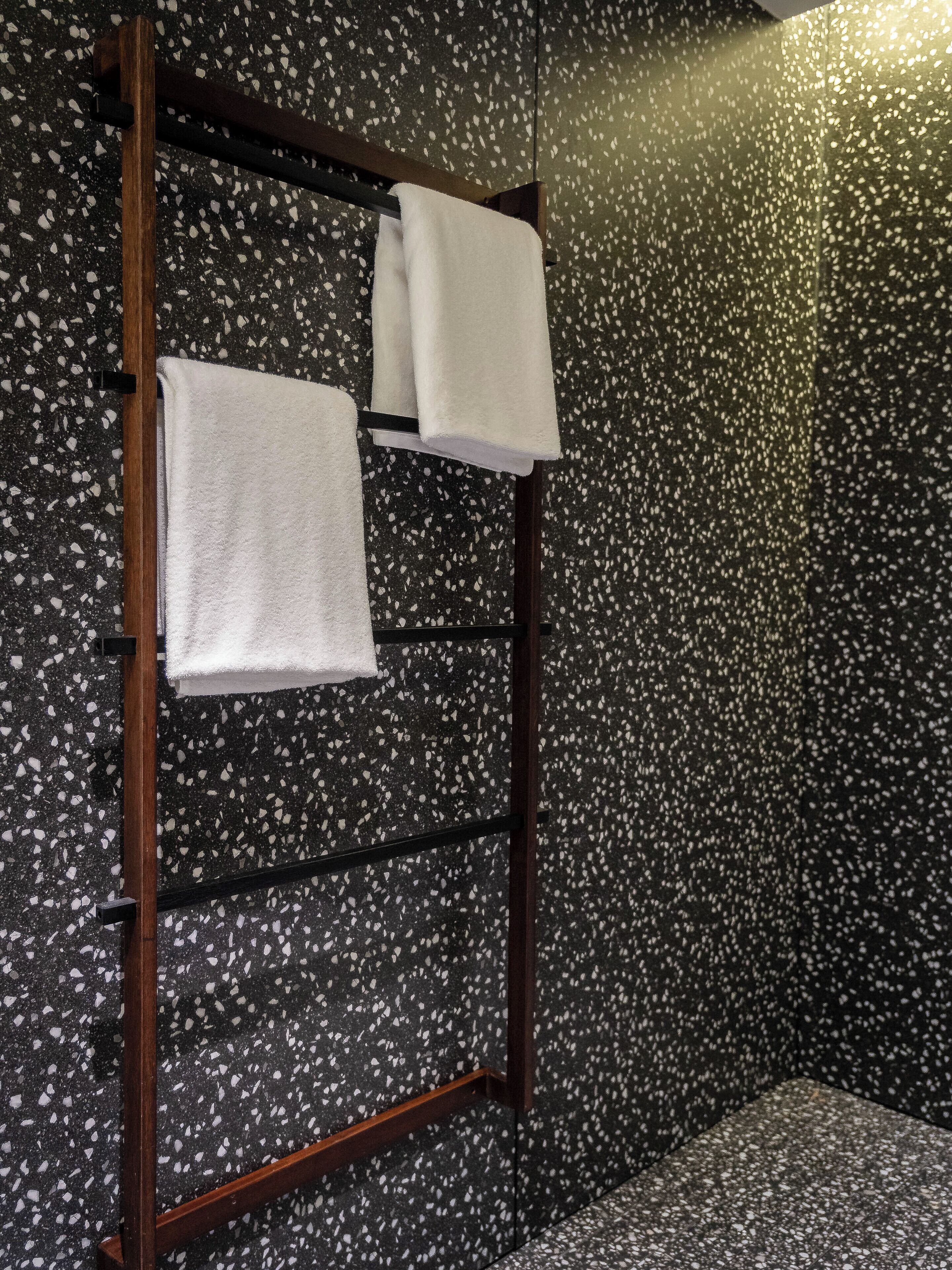 Un baño con un toallero de madera que sostiene dos toallas blancas. La pared tiene un diseño con motas.
