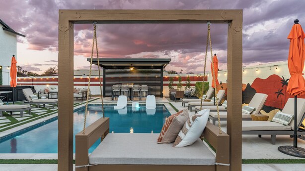 A poolside area with a swing chair, lounge chairs, and umbrellas. - Scottsdale 7-BR Oasis: Speakeasy, Pickleball, Golf (Scottsdale)