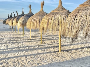 A row of thatched umbrellas on a sandy beach.