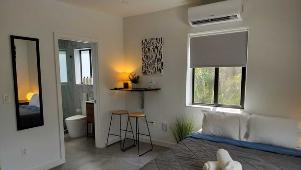 A modern hotel room with a bed, a bathroom, a small seating area, and a window with a view. - Style and comfort in one place 5 (Miami)