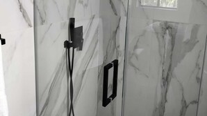 A glass-enclosed shower with a handheld showerhead and a wall-mounted control panel. - Style and comfort in one place 5 (Miami)