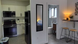 A modern kitchen with white cabinets, a black refrigerator, and a stove. There is a trash bin and a small stool near the kitchen. - Style and comfort in one place 5 (Miami)