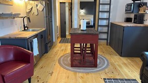Une cuisine compacte avec un plancher en bois, un fauteuil en cuir rouge, une petite table sur laquelle se trouve un rouleau d’essuie-tout et un micro-ondes posé sur une étagère.