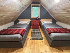 Une chambre avec deux lits, une commode rouge, une fenêtre et un plafond en bois.