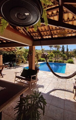 Un patio couvert avec un hamac, une piscine et des sièges d’extérieur.