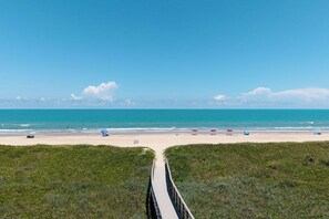 A beach with a wooden boardwalk leading to the shore, clear blue sky, and calm sea.