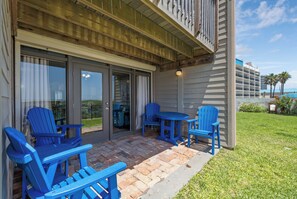 A patio with blue Adirondack chairs and a table, a sliding glass door entrance, and a view of the ocean.