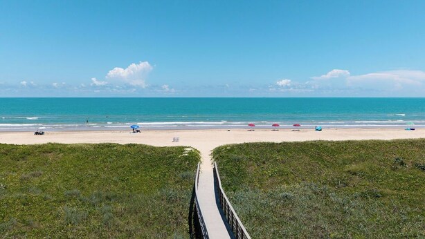 A beach with a wooden boardwalk leading to the shore, clear blue sky, and calm sea.