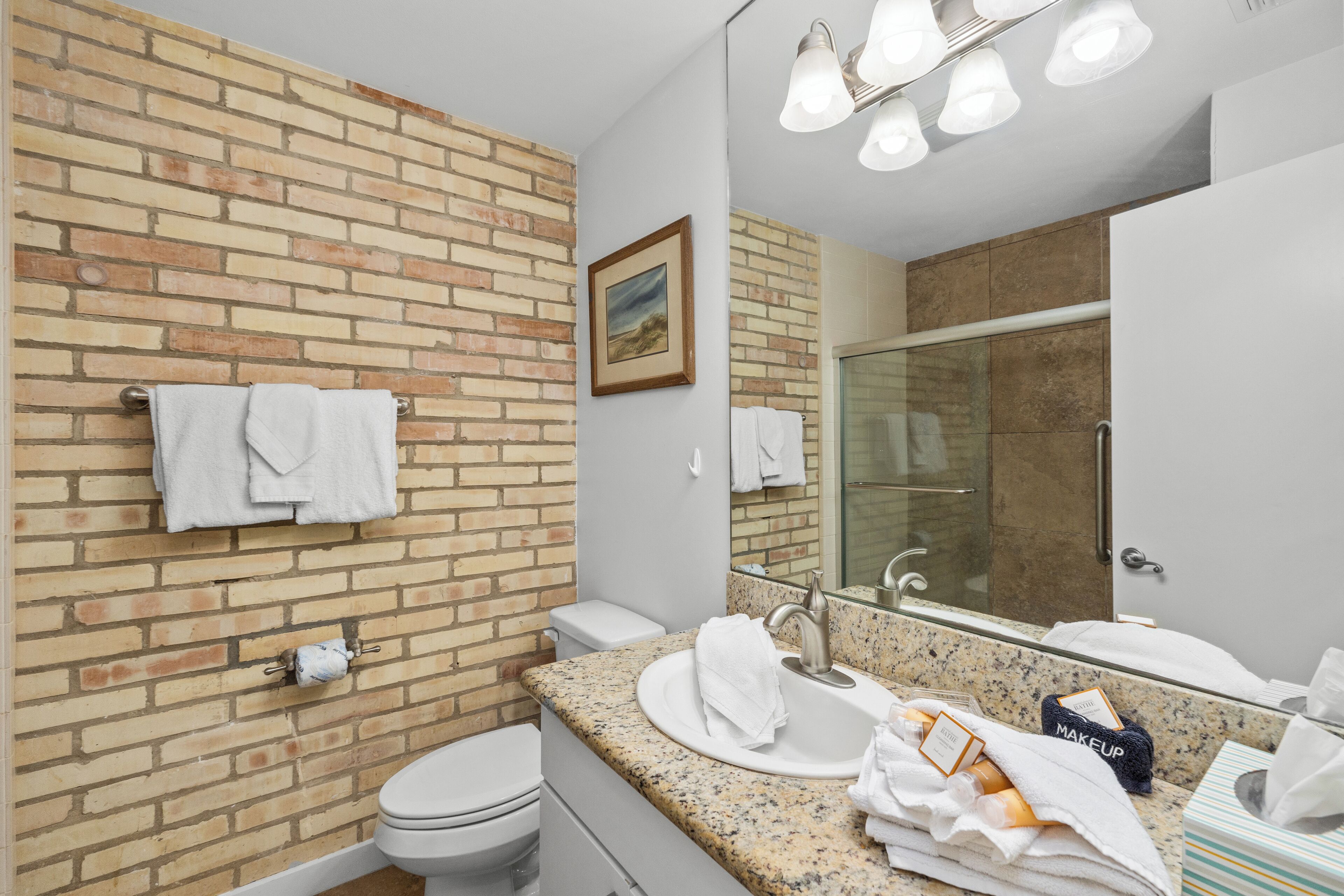 Un baño con pared de ladrillo, un lavabo con espejo y un inodoro.