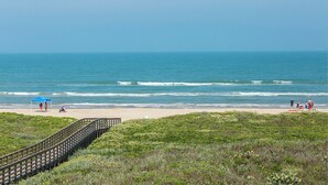 A beach with a wooden boardwalk leading to the shore, a clear blue sky, and the ocean. - Charming 2-Bedroom Condo. Unbeatable Beach Access! (South Padre Island)
