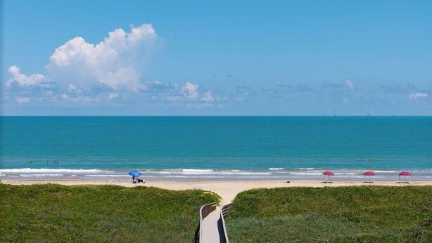 A beach with a clear view of the ocean, a sandy path, and several umbrellas. - Soothing Seaside Comfort in a 2-Bedroom Escape (South Padre Island)
