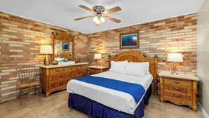 A bedroom with a large bed, wooden headboard, two nightstands, a ceiling fan, and a brick wall. - Soothing Seaside Comfort in a 2-Bedroom Escape (South Padre Island)
