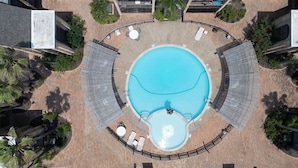An aerial view of a hotel with a central swimming pool surrounded by lounge areas and palm trees. - Soothing Seaside Comfort in a 2-Bedroom Escape (South Padre Island)