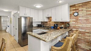 A kitchen with white cabinets, a stainless steel refrigerator, a granite countertop, and a brick accent wall.