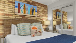 A hotel room with a brick wall, a bed with striped pillows, and a beach-themed painting above the bed.