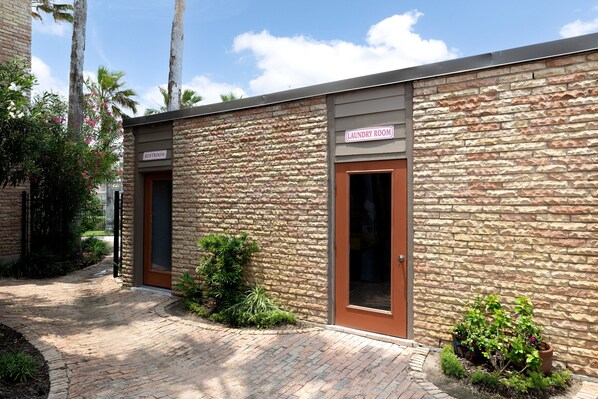 A building with a stone facade, a sign indicating a laundry room, and a restroom. - Beachfront Bliss in a Cozy, Family-Friendly Condo (South Padre Island)