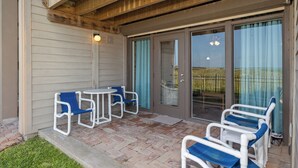 Un patio exterior con zona de estar techada, una puerta que da a un vestíbulo cubierto y vistas del paisaje circundante.