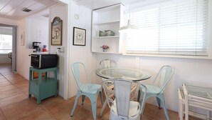 Une cuisine avec une table à plateau en verre, des chaises de couleur turquoise et un meuble de rangement turquoise.